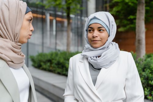 Free Two women wearing hijabs engaging in conversation outside a modern building. Stock Photo