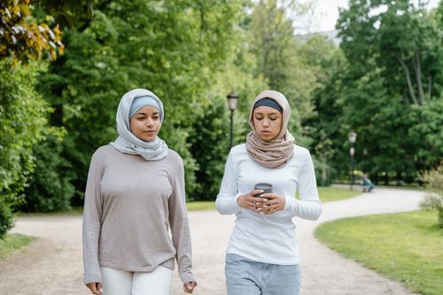 Free Two young Muslim women in hijabs walking in a lush green park, enjoying a casual conversation. Stock Photo