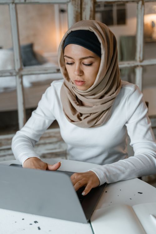 Free A young woman wearing a hijab is focused working on a laptop in a cozy indoor setting. Stock Photo