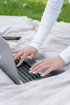 Woman's hands typing on a laptop outdoors on a blanket. Perfect for showcasing portable technology in leisure settings.