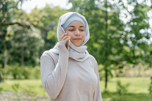 Woman in Beige Long Sleeve Shirt Wearing Hijab Talking on Smartphone