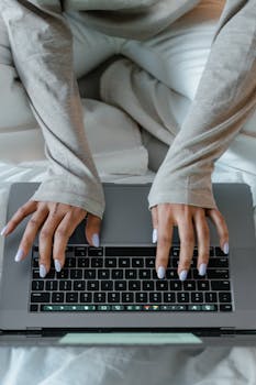 Close-up view of a woman's hands typing on a laptop keyboard while sitting comfortably indoors.