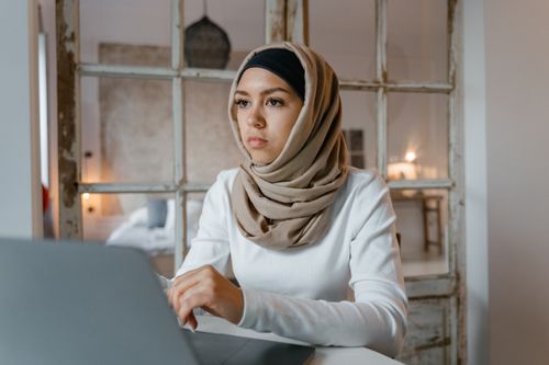 Free A young woman in a hijab concentrates on her work using a laptop in a cozy, well-lit room. Stock Photo