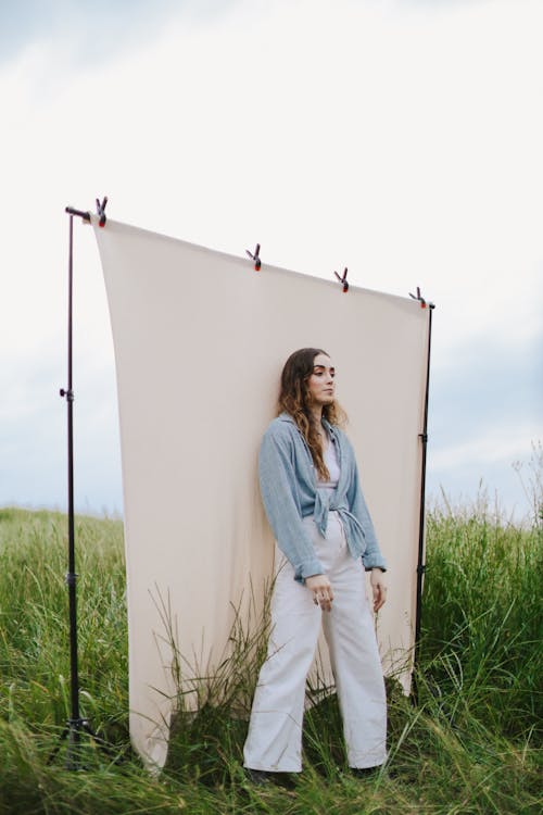 A Woman in Blue Denim Jacket and White Pants Standing on Green Grass Field