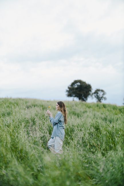 A young woman leisurely walks through a lush green field, enjoying nature's beauty.