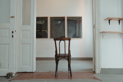 A refined minimalist interior featuring a classic wooden chair, framed art, and soft natural lighting.