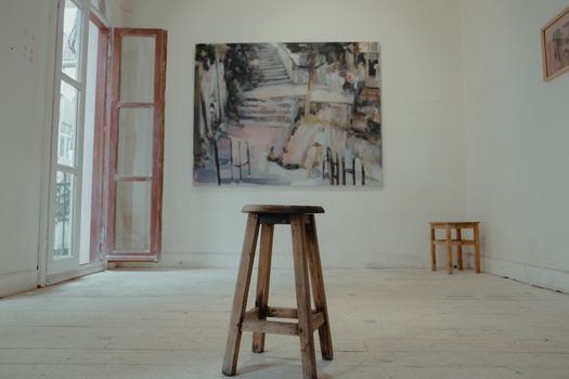 A minimalist art studio featuring an abstract painting and wooden stool, creating a serene artistic ambiance.
