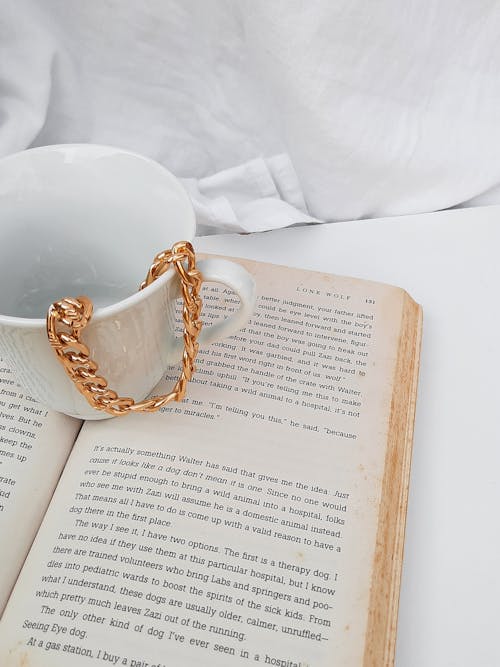 Close-Up Photo of a White Ceramic Mug with a Necklace on Top of a Book