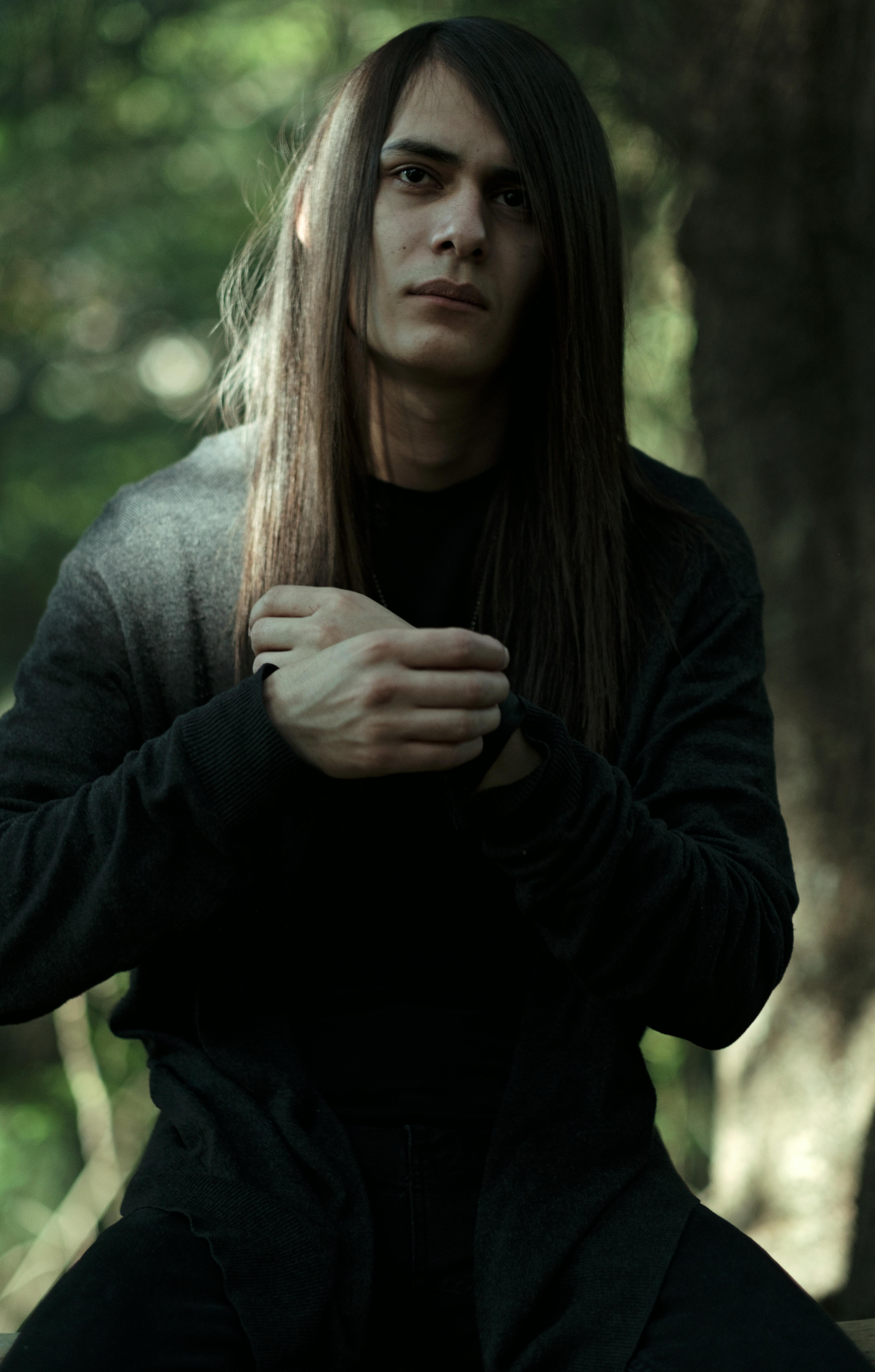 Portrait of a young man with long hair in a serene forest environment, expressing deep thought.
