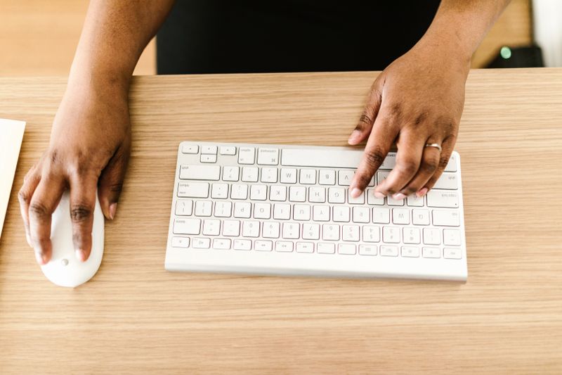 Hands typing on a white keyboard on a wooden desk, ideal for a software download scenario.