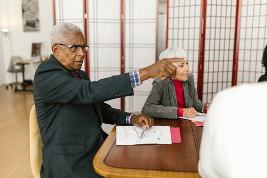 Elderly professionals collaborate in a meeting, discussing documents on a wooden table.