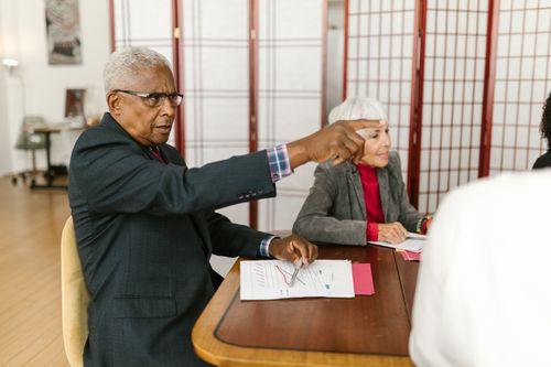 Free Elderly professionals collaborate in a meeting, discussing documents on a wooden table. Stock Photo