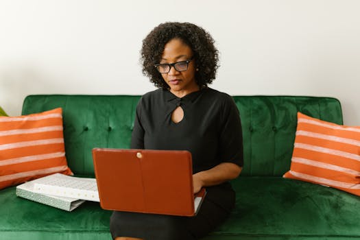 Focused African American woman sitting on a sofa using a laptop at home office.