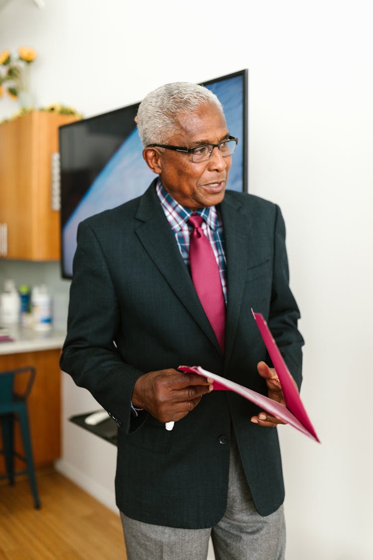 An Elderly Man In Black Suit Holding A Folder