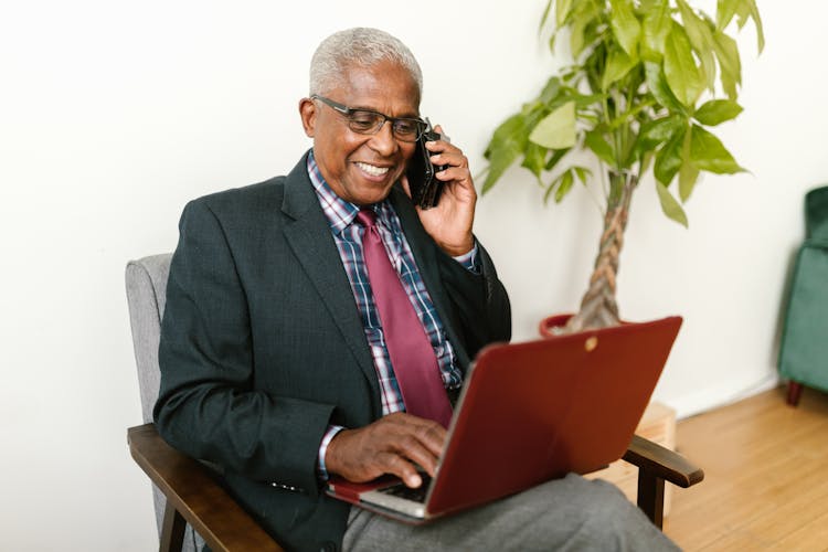 An Elderly Man Using A Laptop While Talking On Phone