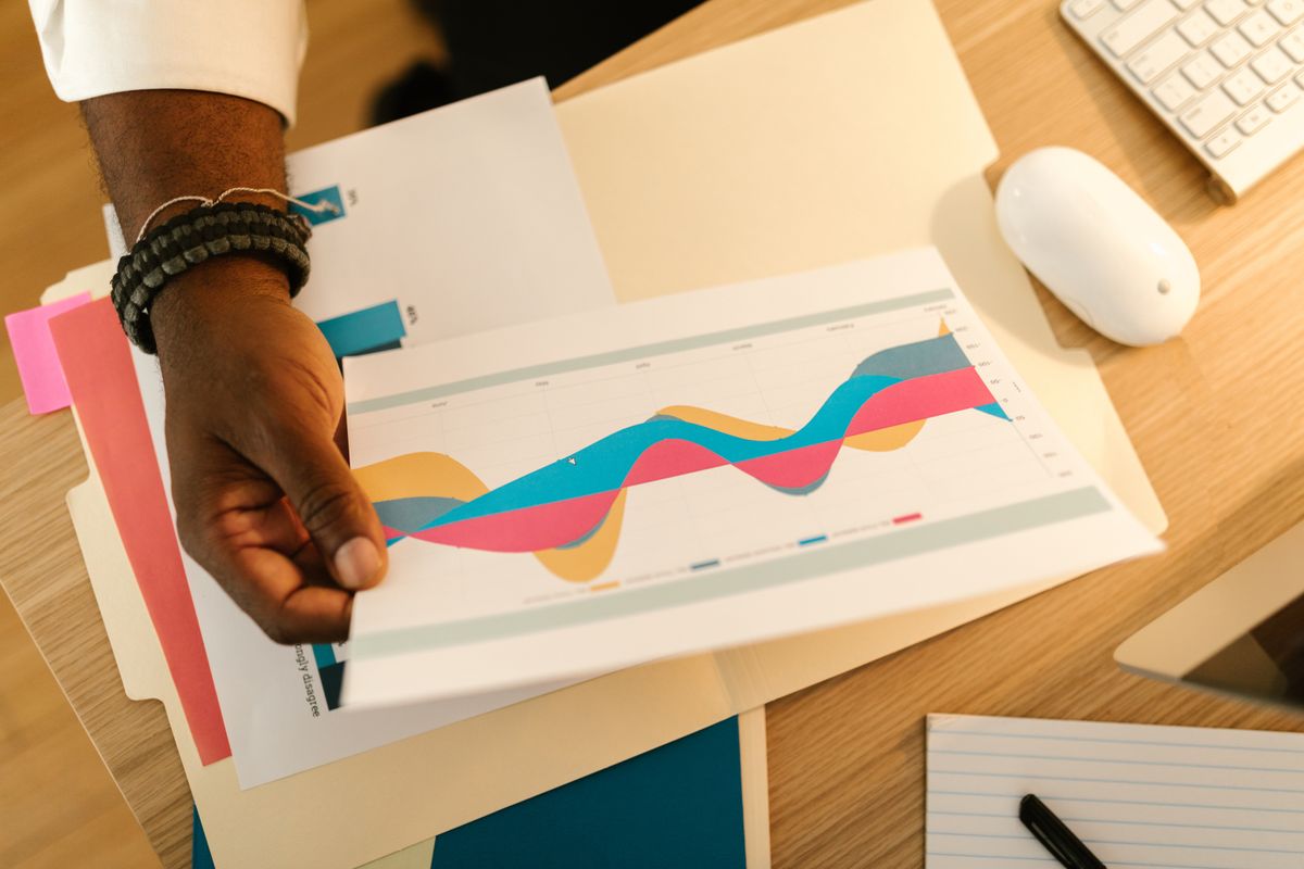 A printed reporting chart held over a wooden desk — photo by RDNE Stock project on Pexels