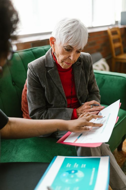 Free An elderly woman in a grey suit discusses reports with a colleague indoors. Stock Photo