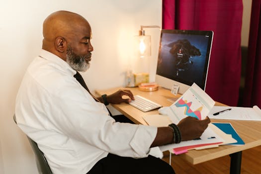 A mature professional working on business charts at a desk with a computer in an office setting.