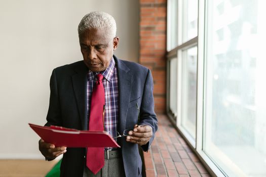Elderly man in formal attire reviewing documents indoors with natural light.