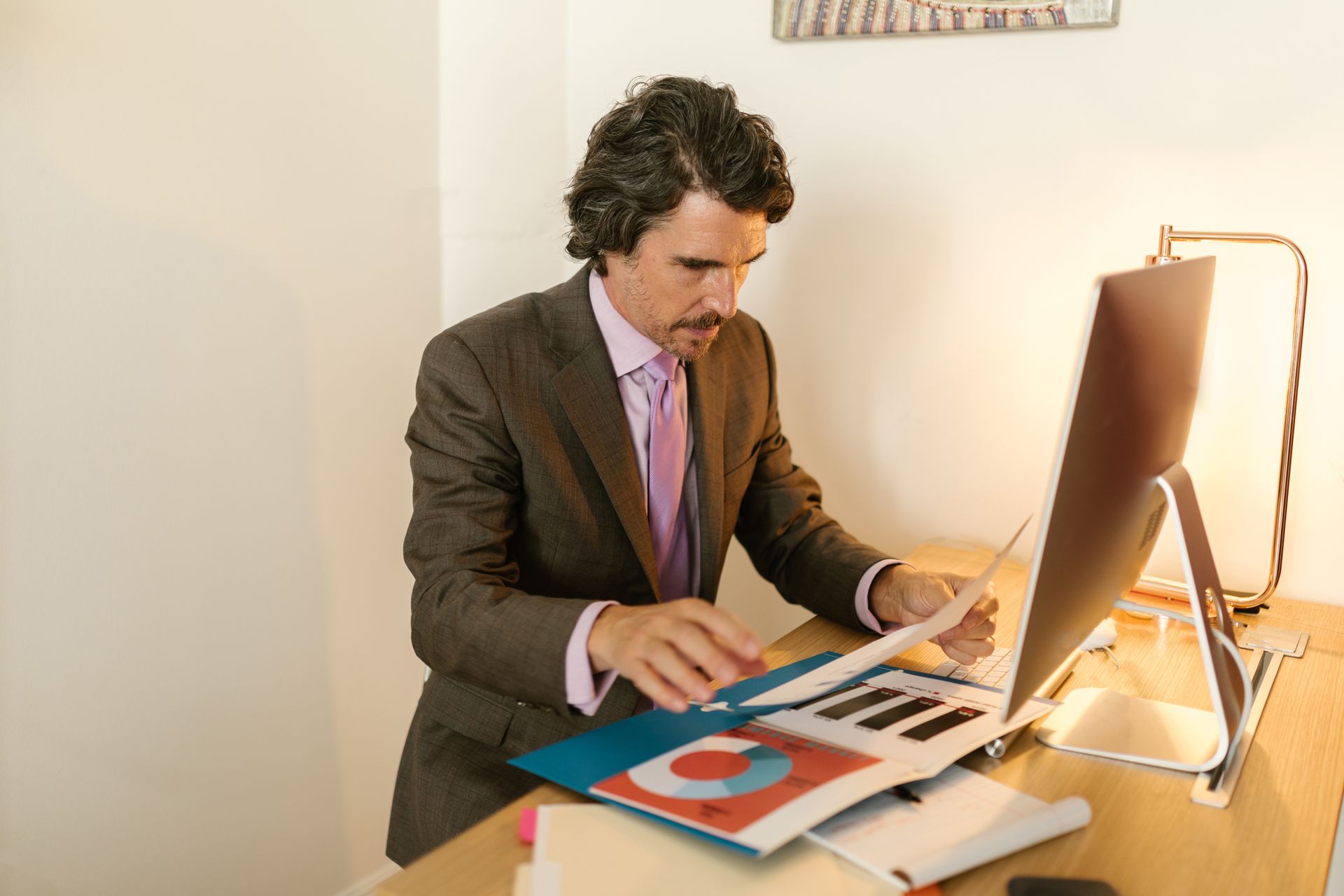 Man in Suit Sitting on His Desk while Looking at the Document he is Holding