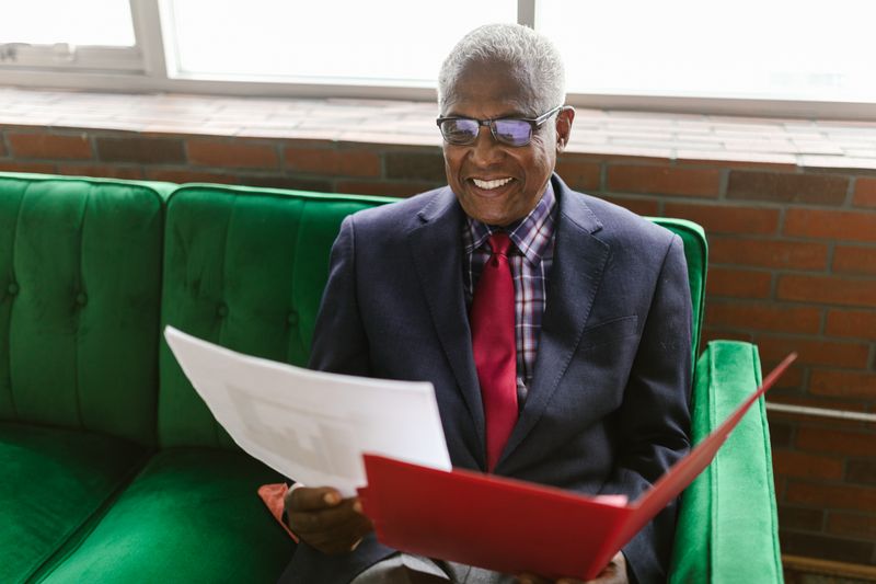 An elderly man in a suit smiling on his living-room couch