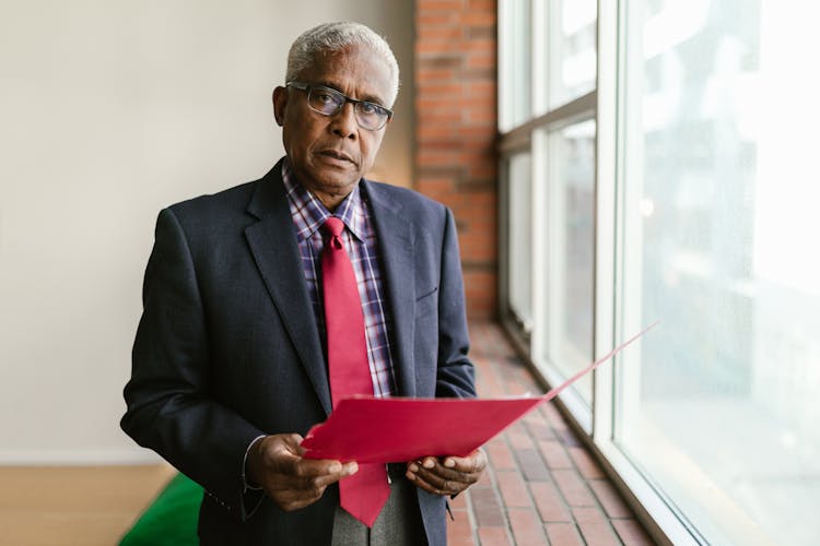 Gray Haired Man Holding A Red Folder 