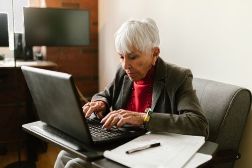 Free Senior woman with gray hair working on a laptop in a cozy home office setting. Stock Photo