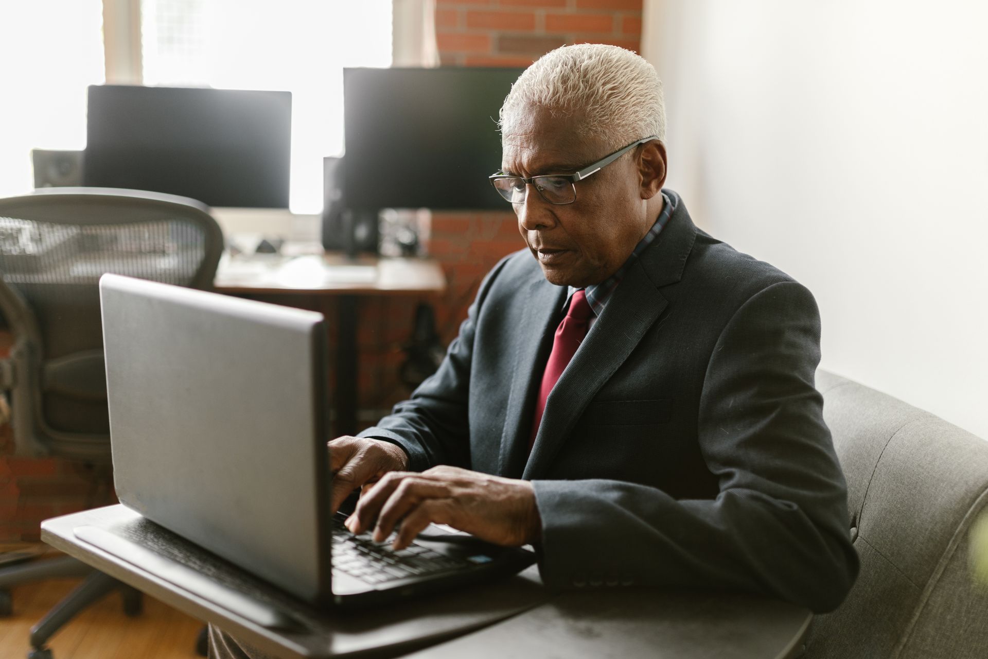 Elderly man in business attire using a laptop in a modern office setting.