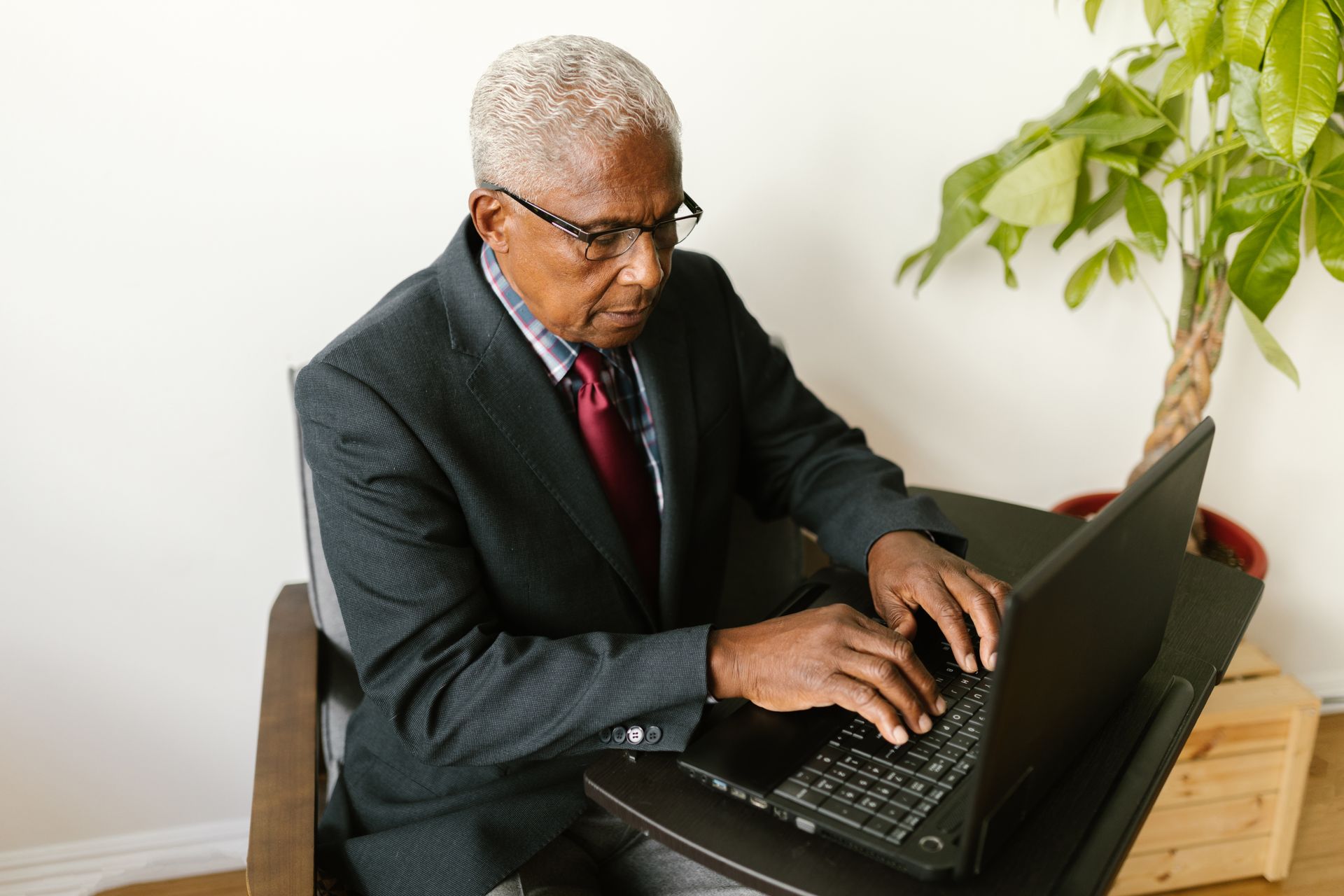 Elderly man in a gray suit working on a laptop at an office desk.
