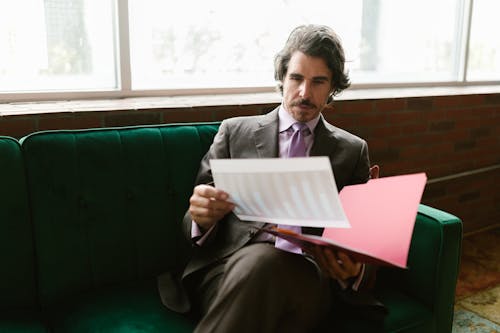 Man in Brown Suit Looking at the White Paper