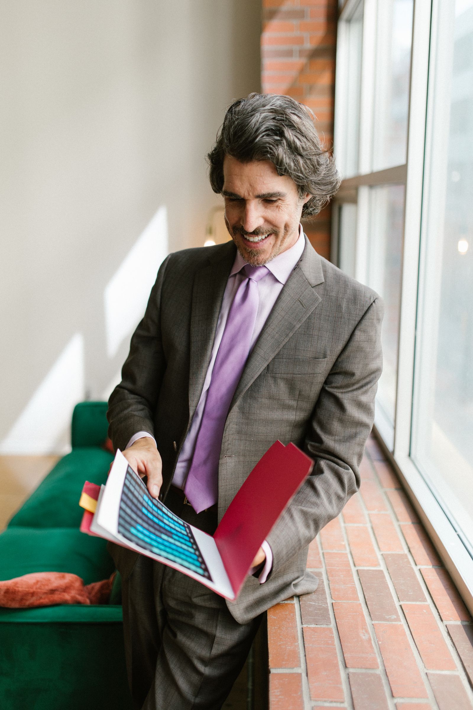 A man in a grey suit holding documents in an office