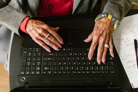 Close-up of senior woman's hands typing on laptop with rings and manicured nails.
