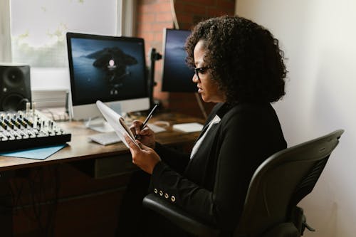 Free Curly Haired Woman in Front of a Computer Monitor Seriously Writing on a Paper Stock Photo