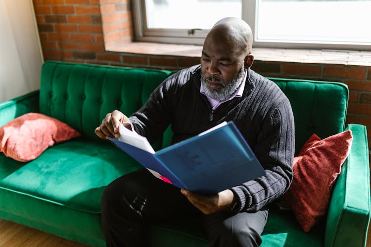 A Man Sitting On Green Couch While Looking Documents