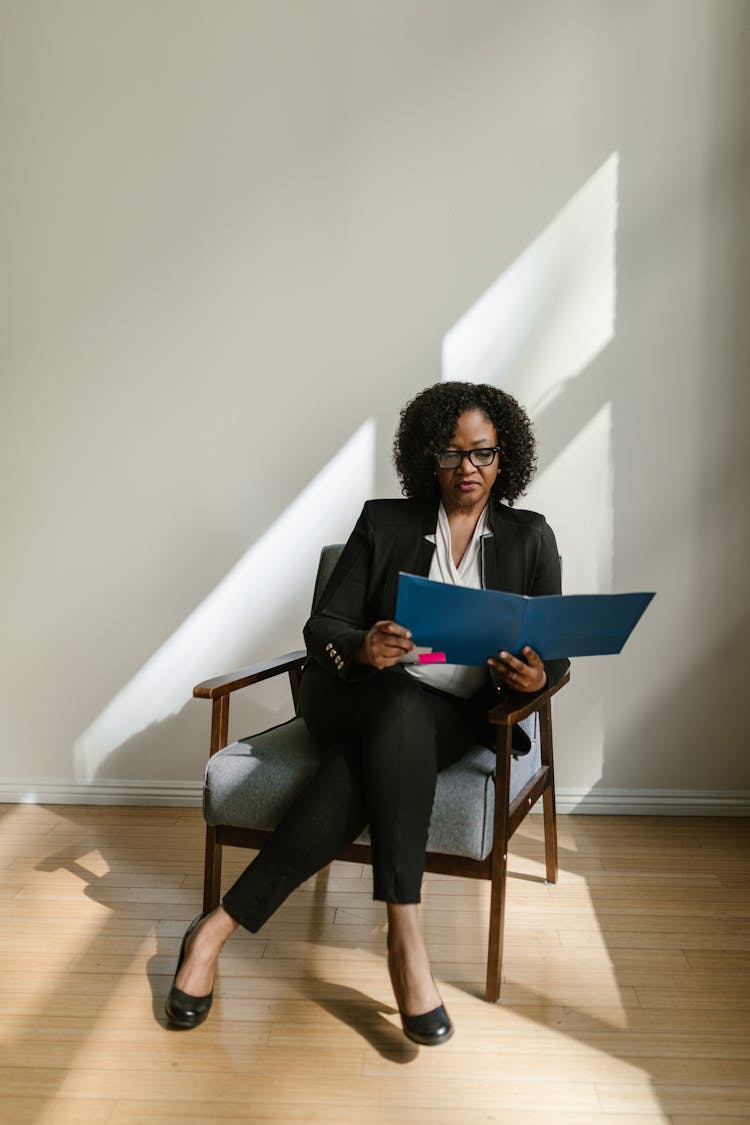 Woman Sitting On A Wooden Armchair Holding A Blue Folder