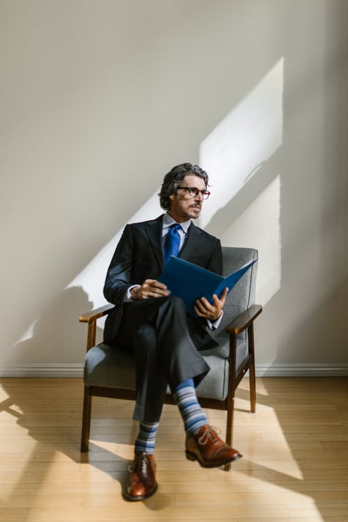 Free Man Wearing Black Suit and Blue Striped Socks Sitting on a Wooden Armchair  Stock Photo