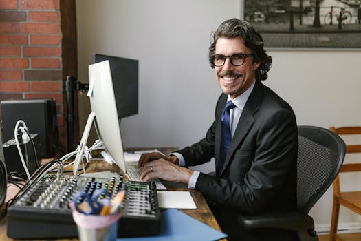 Smiling professional man in office attire typing on a computer in a modern office setting.