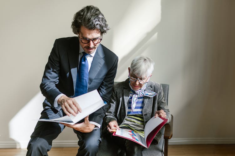 People Sitting Close On A Wooden Armchair Looking At The Papers Inside The Folders