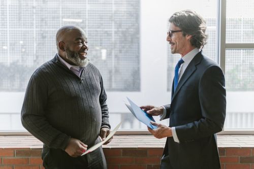 Free Two businessmen in a corporate setting engaging in a friendly conversation indoors. Stock Photo
