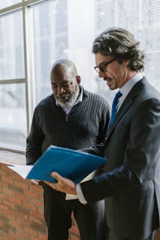 Two senior businessmen in conversation, reviewing documents in a modern office setting.