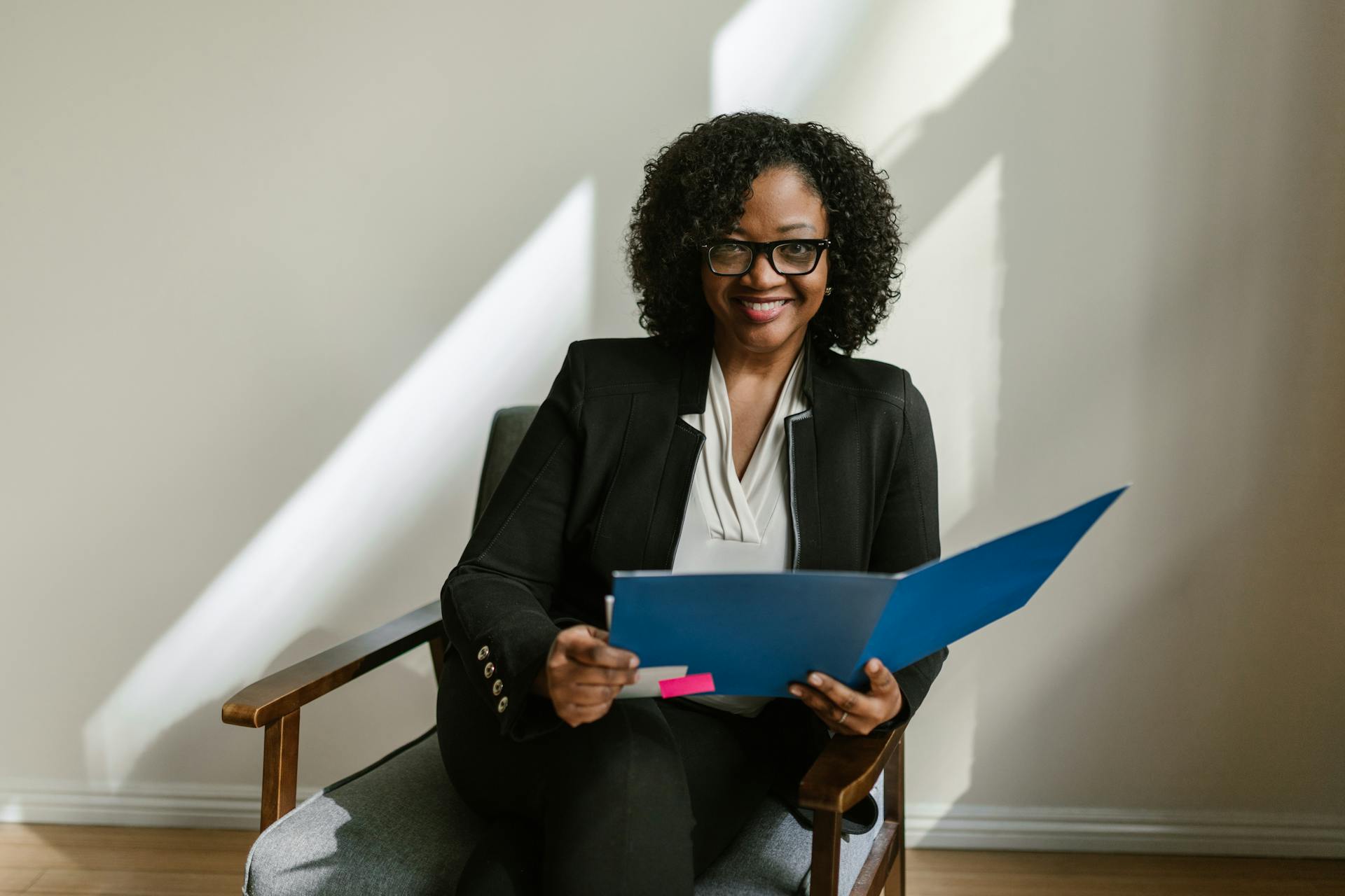 A Woman in Black Blazer Sitting on a Chair Holding Blue Folder