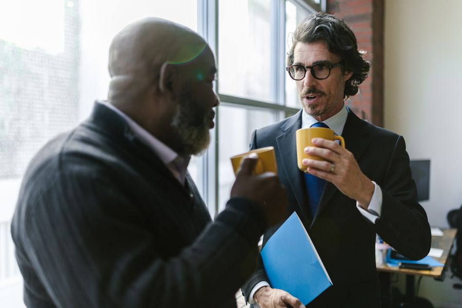 Two colleagues talking over coffee beside an office window, photo by RDNE Stock project on Pexels