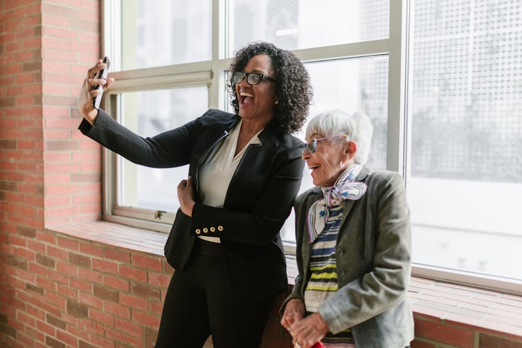 A Woman In Black Blazer Taking Selfie With An Elderly Woman In Gray Blazer