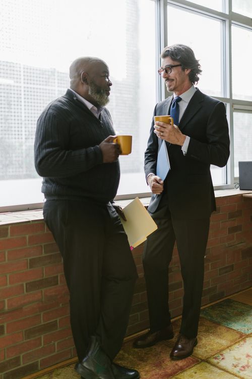 Free Two men in business attire having a conversation, holding coffee mugs indoors. Stock Photo