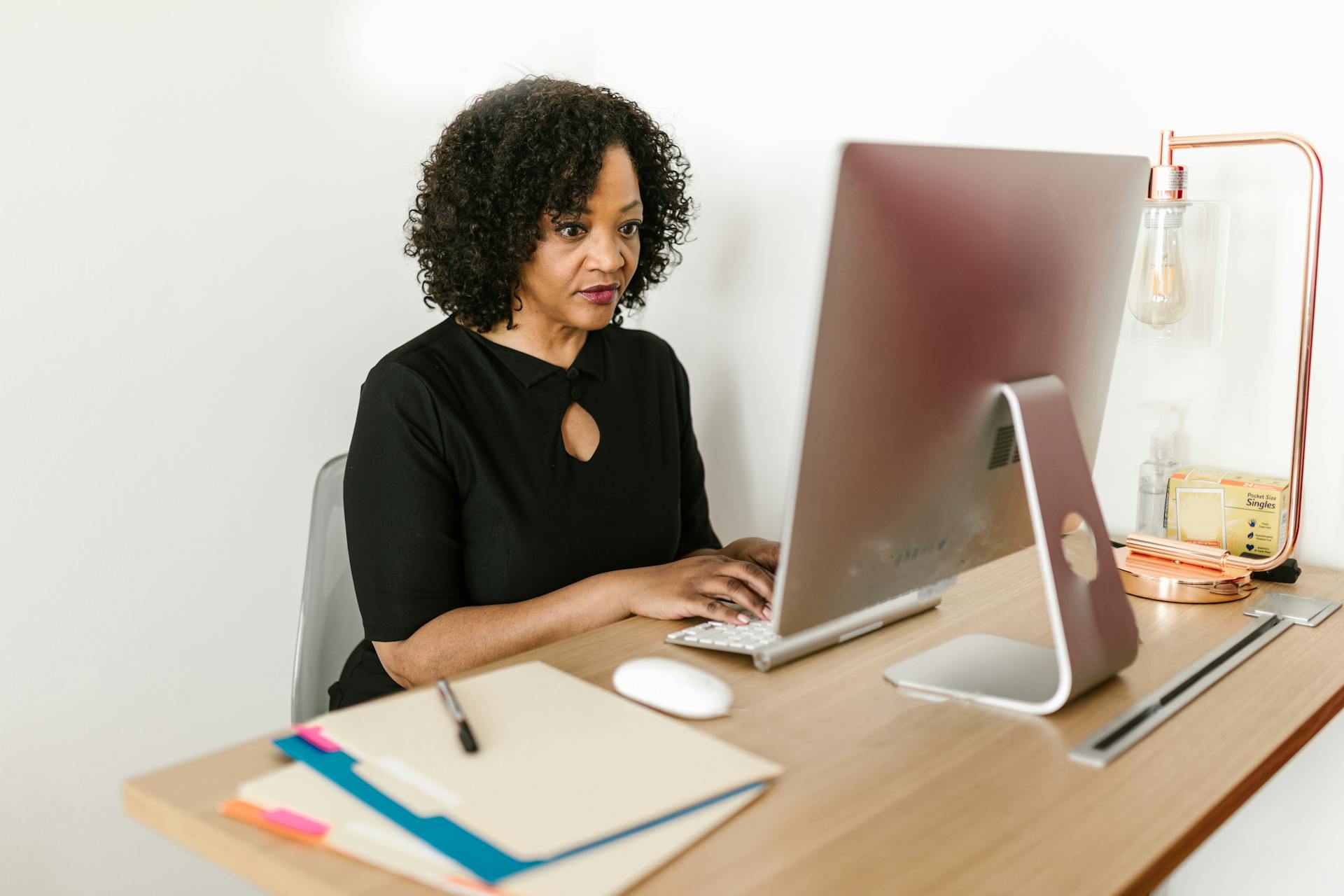 Woman in black attire working on a desktop computer in an office environment.