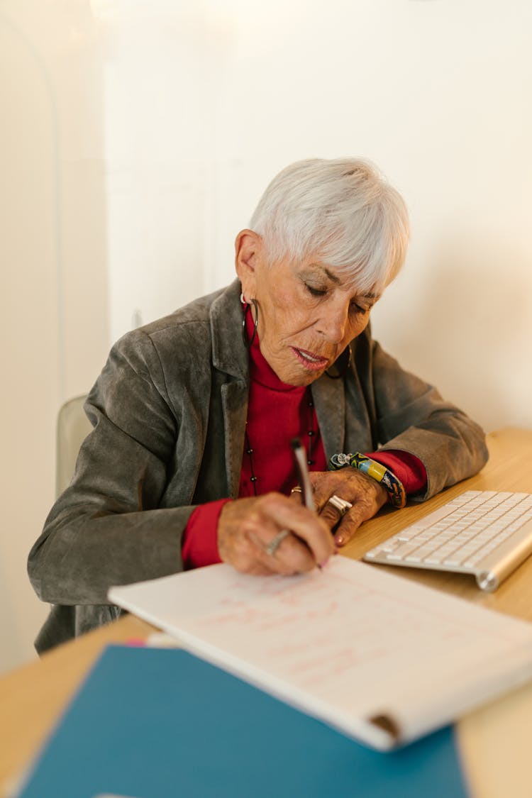 An Elderly Woman In Gray Blazer Writing On Paper