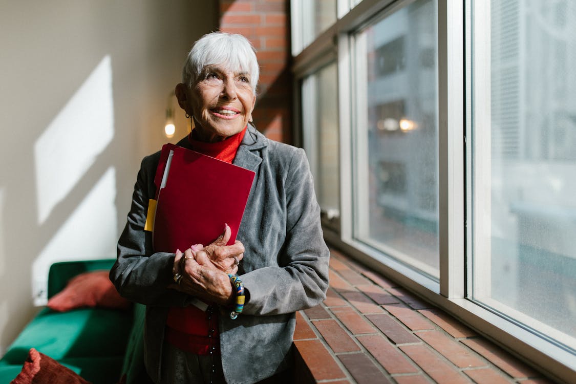 Free Elderly Woman Smiling Holding a Red Folder Stock Photo