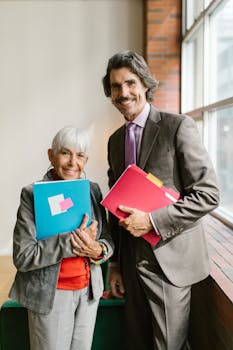 Elderly man and woman smiling with folders in modern office setting.