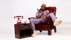 Fashionable man in a purple outfit relaxing on a wooden chair with vintage telephone.