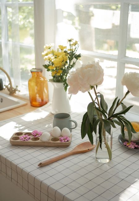 A sunny kitchen setting featuring flowers, eggs, and decor on a table.